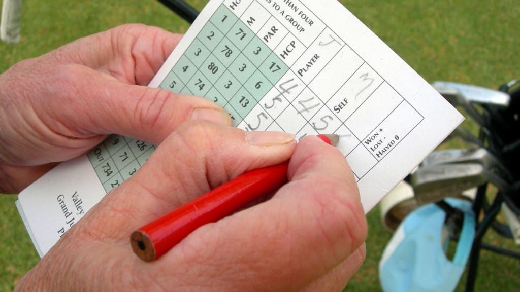 Close-up of a person’s hands holding a red pencil and recording golf scoring on a scorecard, with a golf bag and clubs visible in the background.